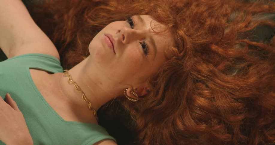 Woman with curly red hair earrings and a necklace lies down on the floor