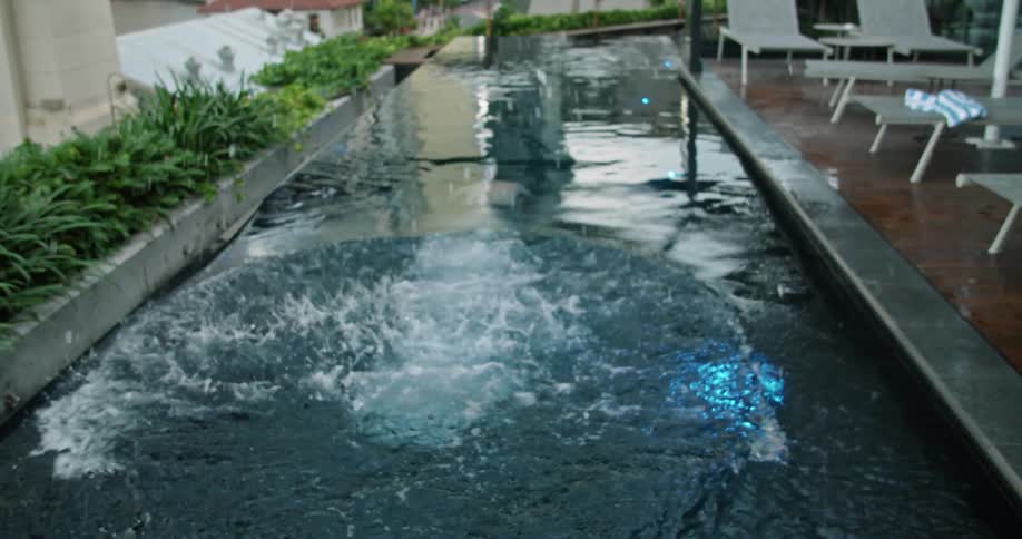 A man stands before a narrow swimming pool atop a building patio before diving in and swimming