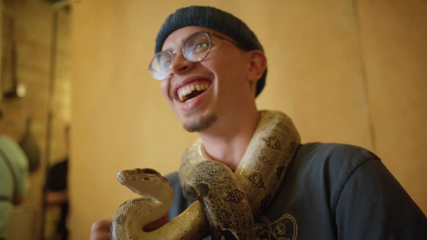A man with a snake wrapped around his neck laughs