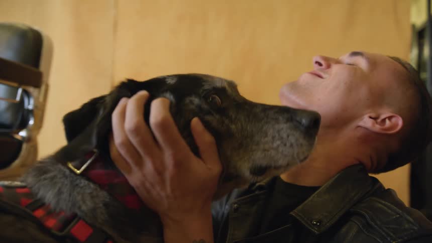 A man in a room playing with a dog with a chair and a wall in the background