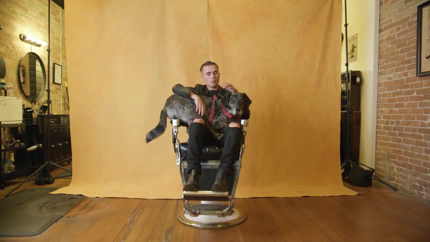 A man is posing in a barber chair with a dog