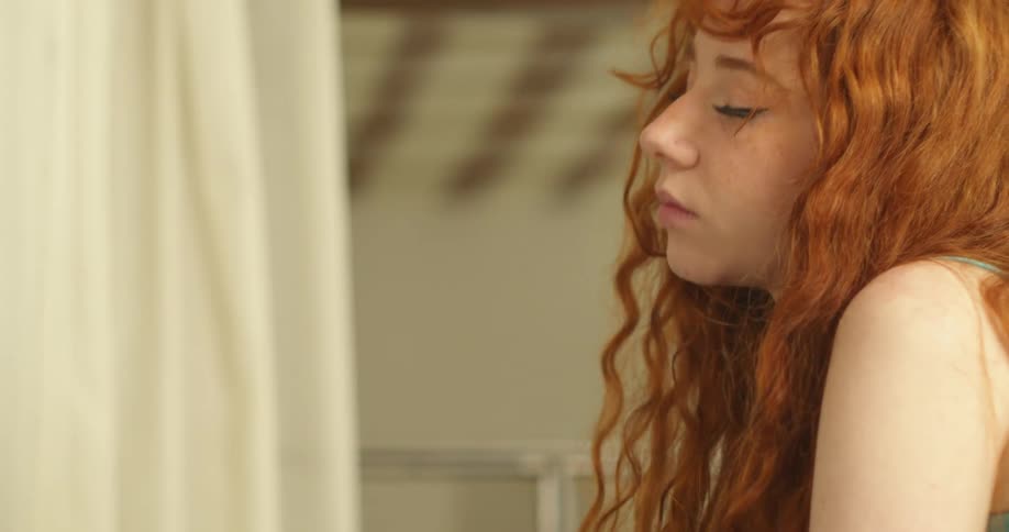 A teenage girl runs her hand down her arm and closes her eyes as she turns her head and looks down