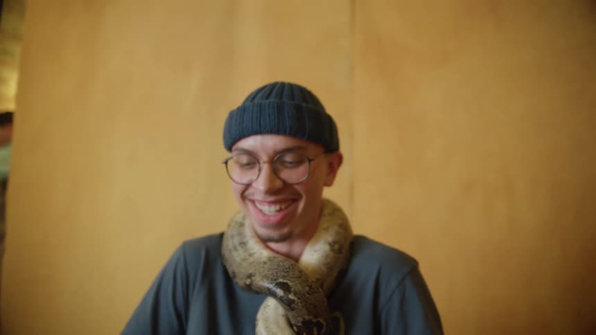 A man with a snake wrapped around his neck sits and laughs