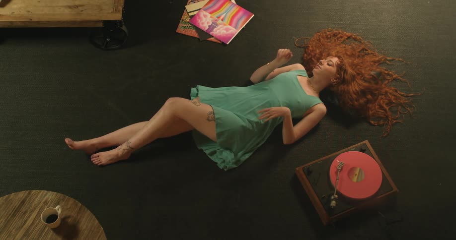 A woman relaxing and listening to music while lying on a floor next to a record player