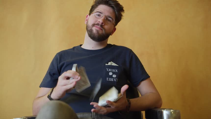 A man sits in a chair and flips playing cards from one hand in to another