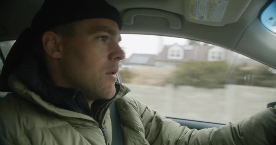 A man drives a car with a nervous look on his face