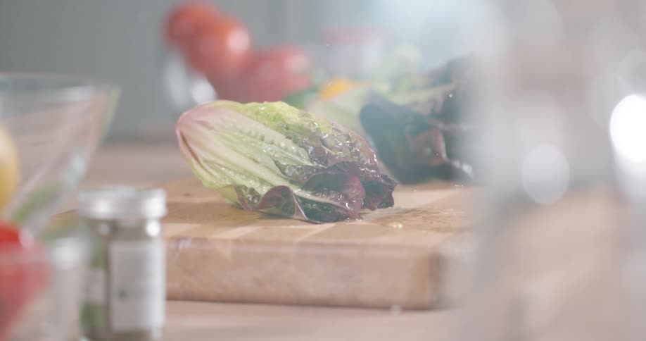 A wet head of lettuce dropping onto a wood cutting board in a kitchen