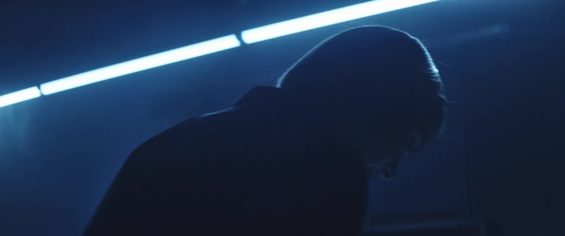 A person in a room with fluorescent lights with a wall in the background