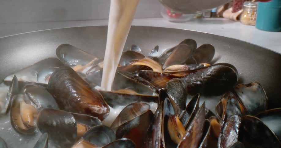 Liquid being poured over seafood cooking in a hot pan