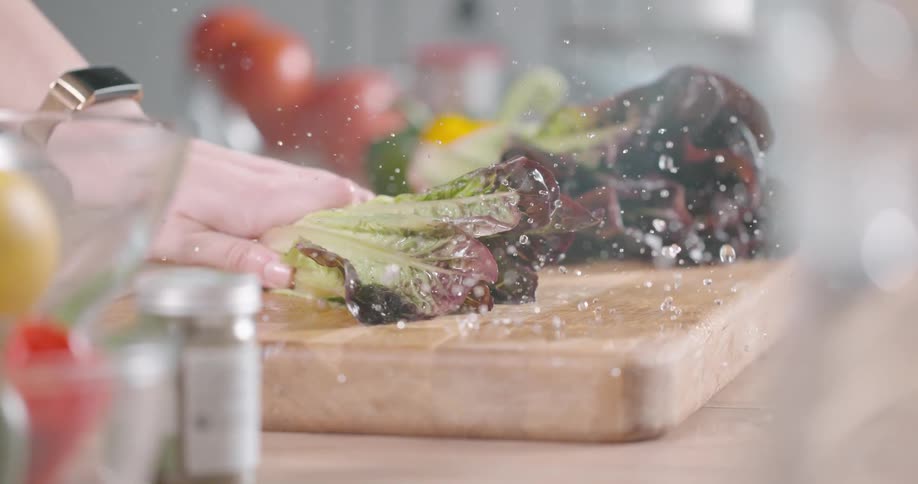 Water droplets spray off of lettuce as a woman smacks it down on a cutting board