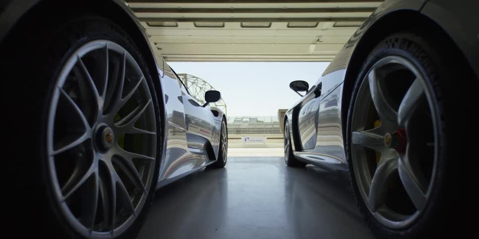 A pair of sports cars parked side by side in a garage during the day