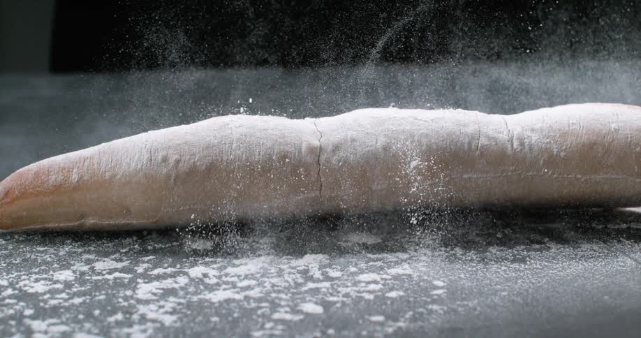 A loaf of bread falling on a table with flour