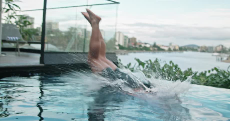 A man dives in to an outdoor pool with the coast and city skyline in the background