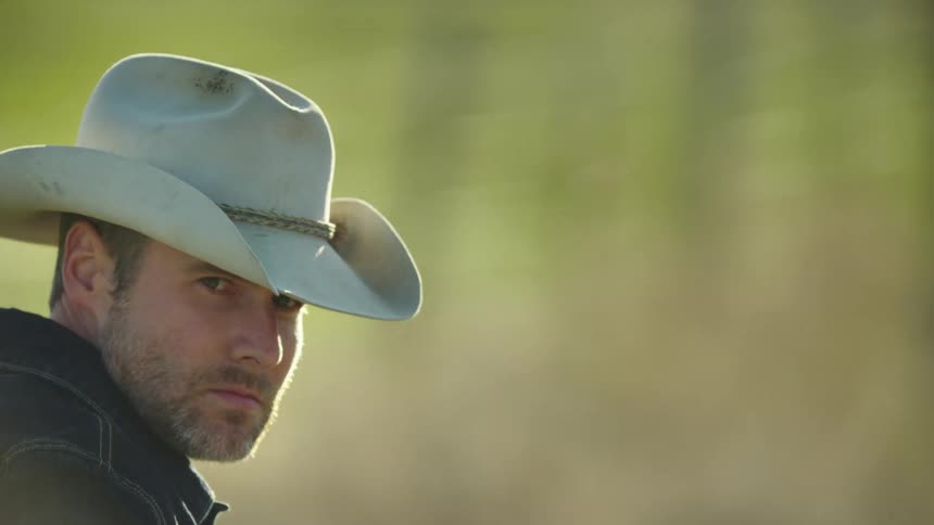 A hard working square jawed man wearing a cowboy hat turns his head to look over his right shoulder as he contemplates hard work and future projects
