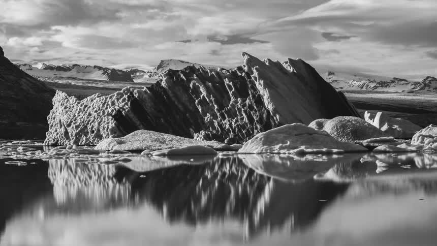 Iceberg and ice floating across the water under a cloudy sky