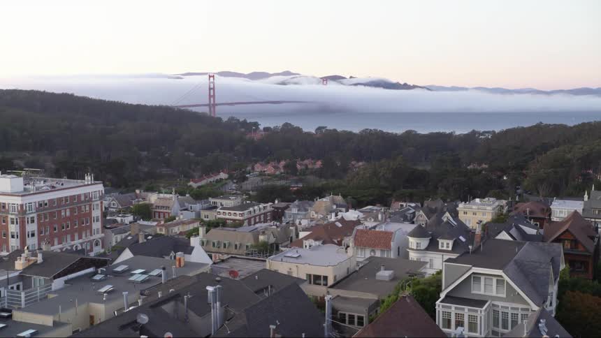 A neighborhood with buildings and trees with a bridge the sky and clouds in the background
