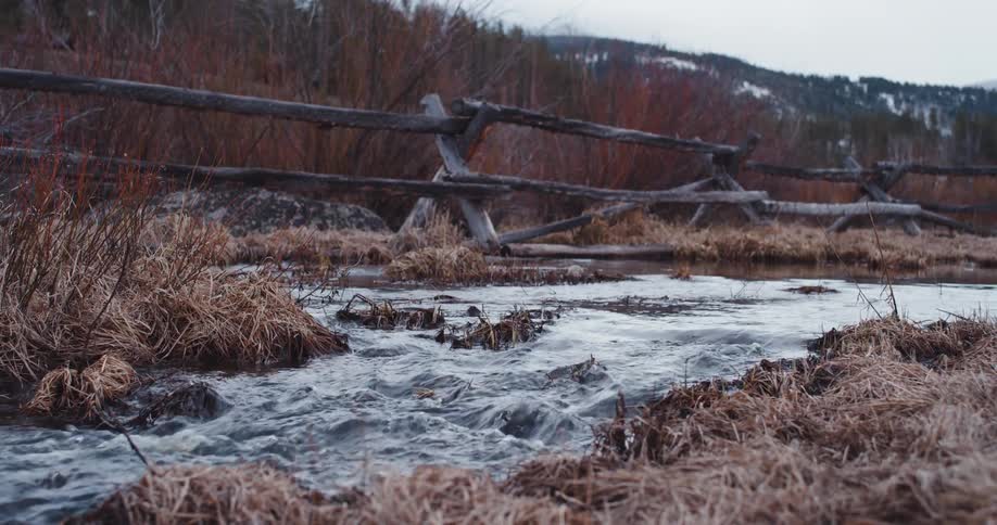 A stream flowing through a rural landscape near a wood fence