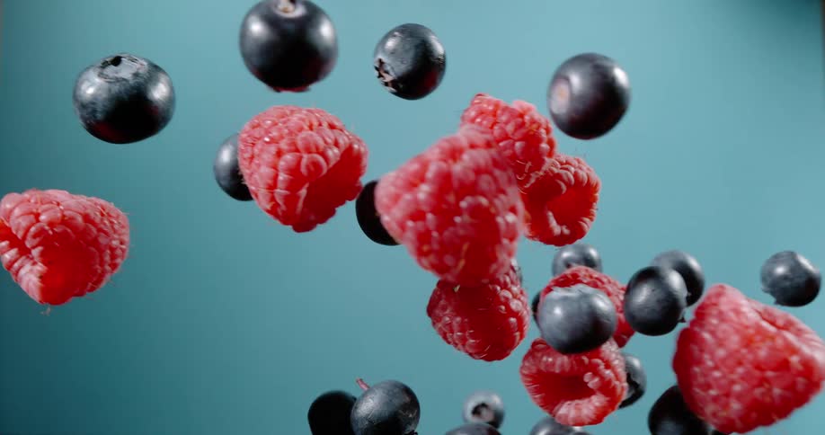 Red and black berries clashing in the air in front of a blue background