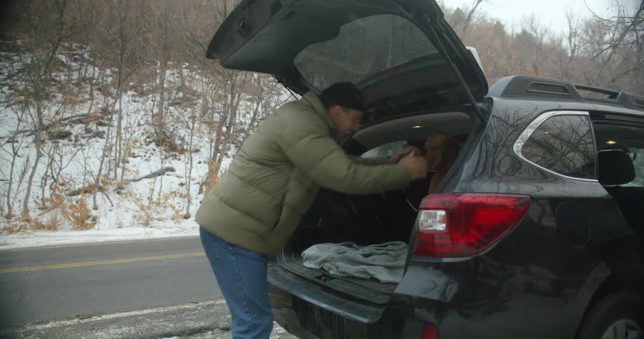 A man opens up the back of his car and pets his dog