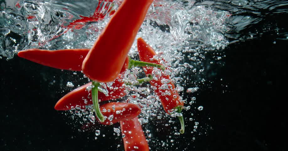Chili peppers falling into water with bubbles with a black background
