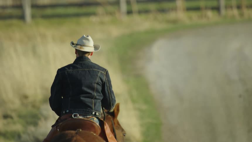 Tight shot of a lone cowboy riding down a dirt path at sunset on a Buffalo ranch feeding america