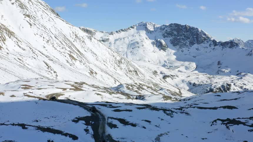Trucks travel on road alongside a snow covered mountain range