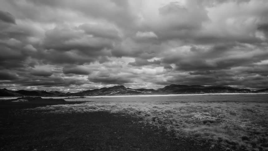 Black and white time lapse of clouds rolling over the fields next to the mountains