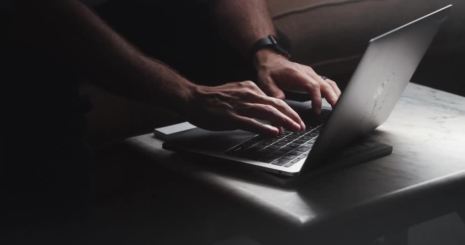 A man typing on a laptop while sitting on a sofa