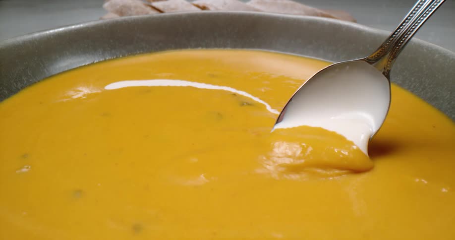 Spoon mixing white and yellow cream in a soup bowl