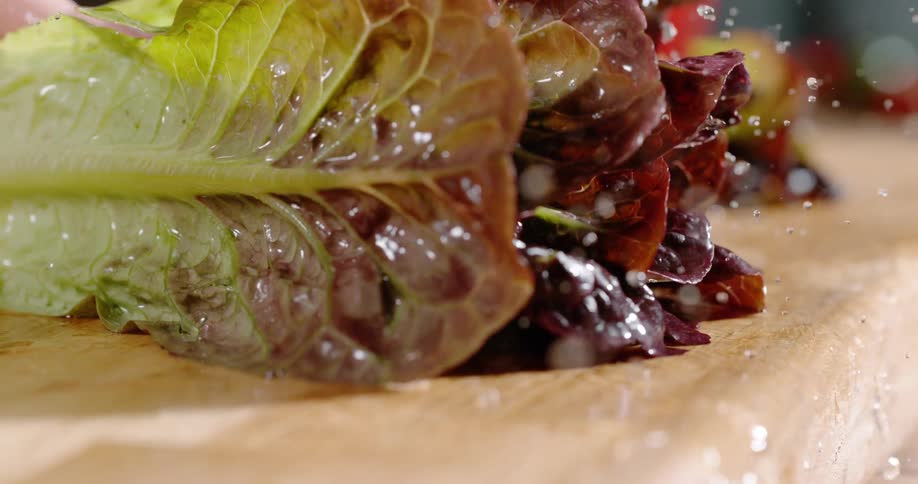 A person placing wet romaine lettuce with water droplets on a cutting board