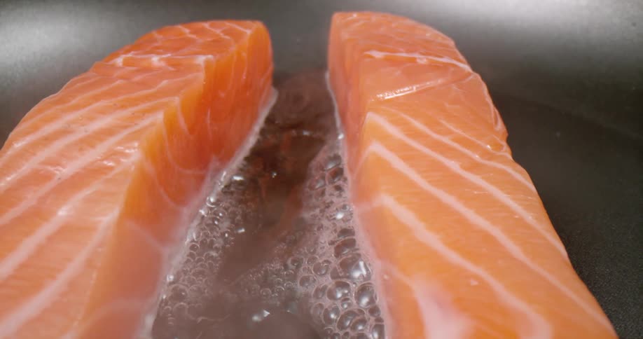 Salmon cooking in a frying pan with oil bubbling and smoke