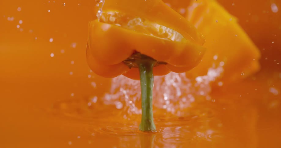Falling sliced orange pepper splashing water