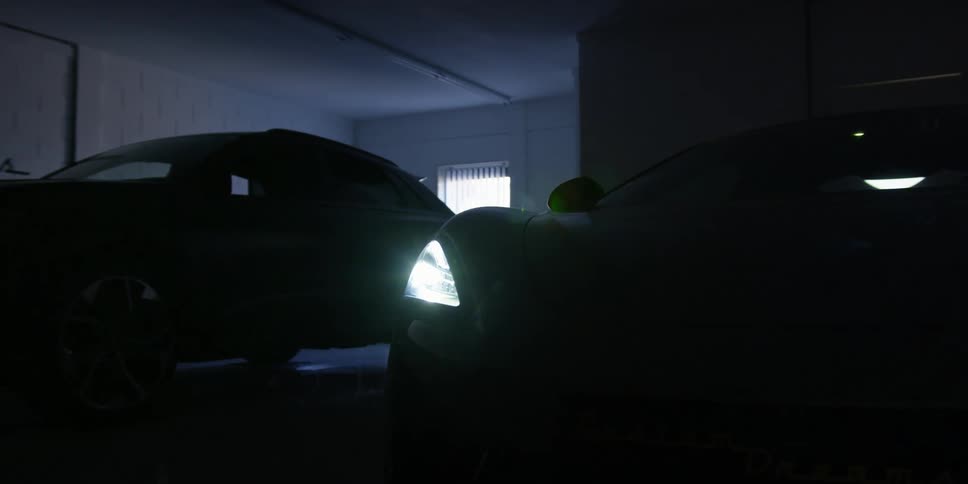 Two vehicles in a garage with a ceiling wall and window in the background