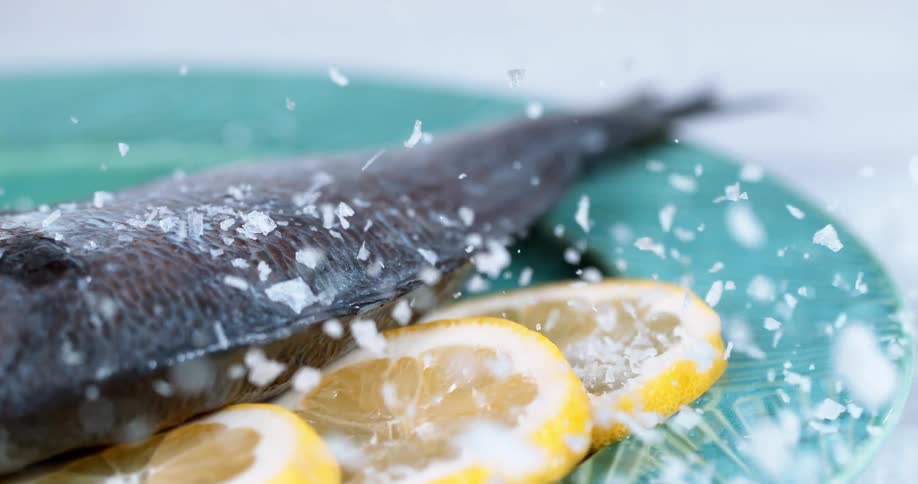A dish with a fish and lemon slices with salt being sprinkled on it