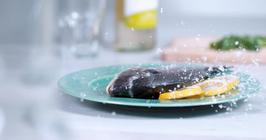 A person throws seasoning on a fish for a photo shoot