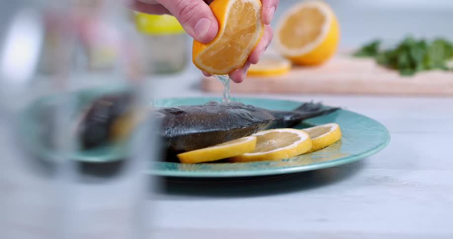 Hand squeezing orange juice over a fish served on a blue dish