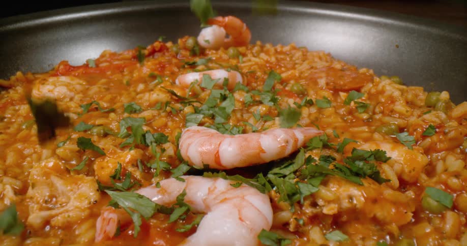 Herbs and shrimp falling in to a pan of food cooking