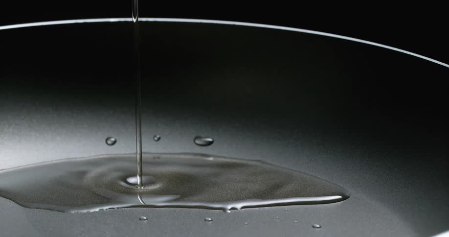 Cooking oil dripping over a pan against a blakc background