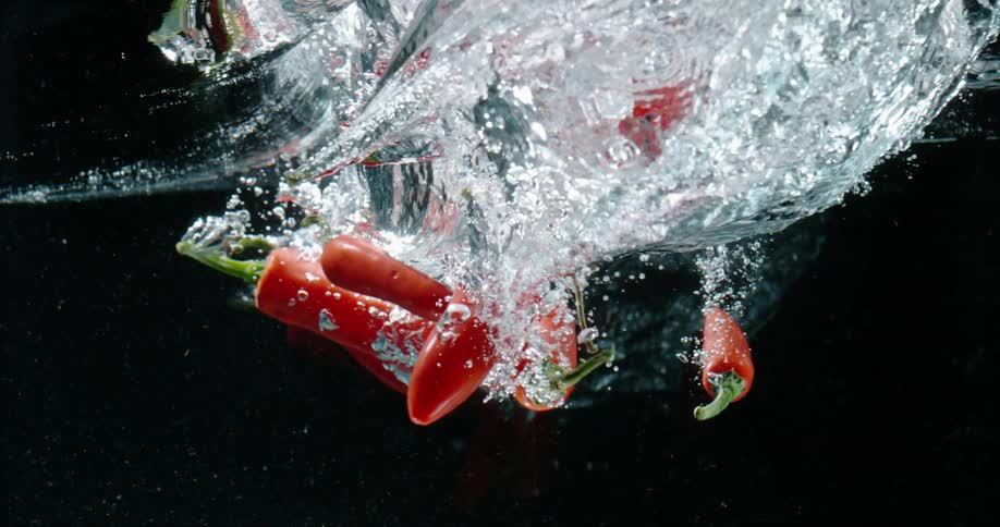 Chili peppers falling into water with bubbles with a black background