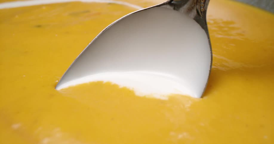 A spoon stirring cream into a soupy liquid