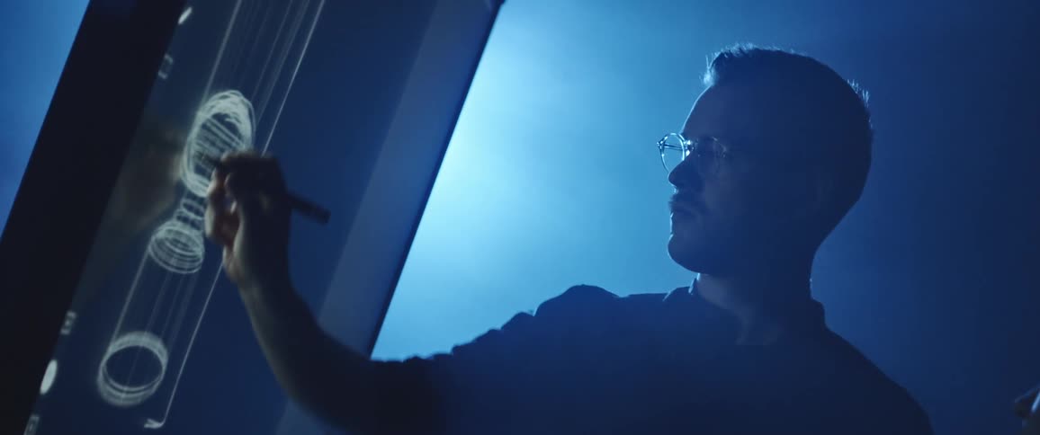 Man drawing a design on an interactive screen inside a dimly lit room under blue lights