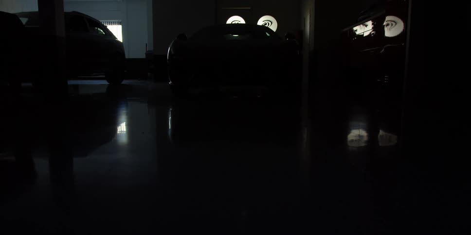 A luxury sports car is in a dark garage when the parking lights flash and the headlights turn on