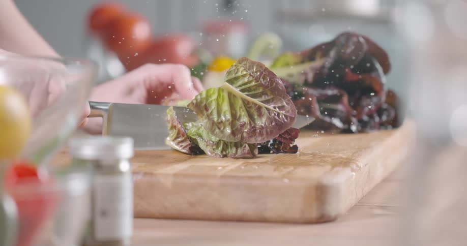 A person slices leafy vegetables over a chopping board with a kitchen knife