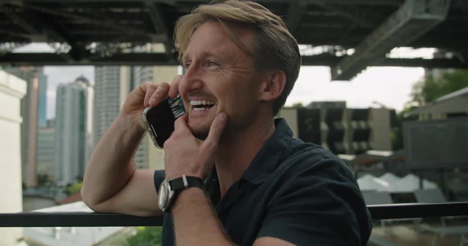 A man stands outside on a city building balcony talking on the phone