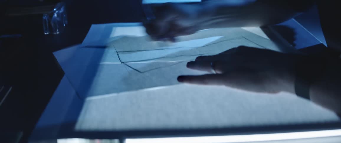 A man with glasses sitting at a desk drawing on a paper with a pen
