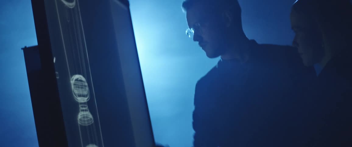 A man uses a stylus to draw on a large screen while a woman stands beside and watches in a dimly lit room