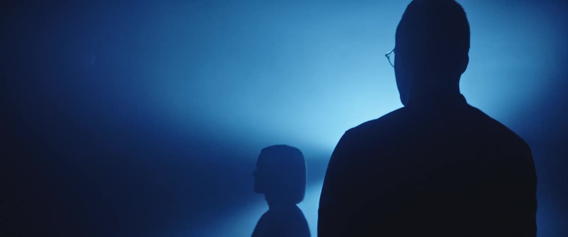 A man and woman silhouetted against a bright light in a foggy room