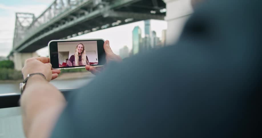 A person video chatting on a smartphone with a river a bridge the sky and clouds in the background