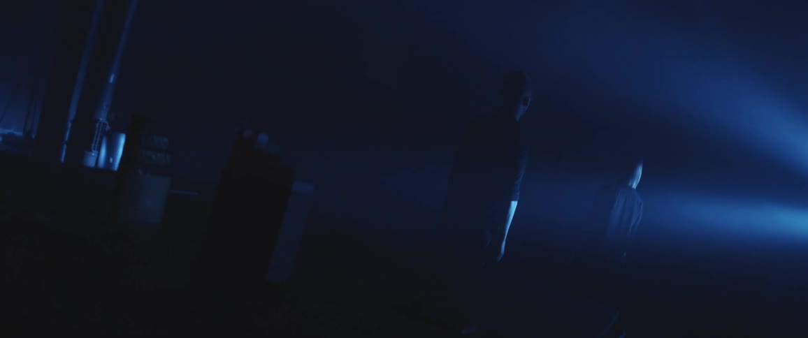 A man and woman stand in a dark room and face a bright flare