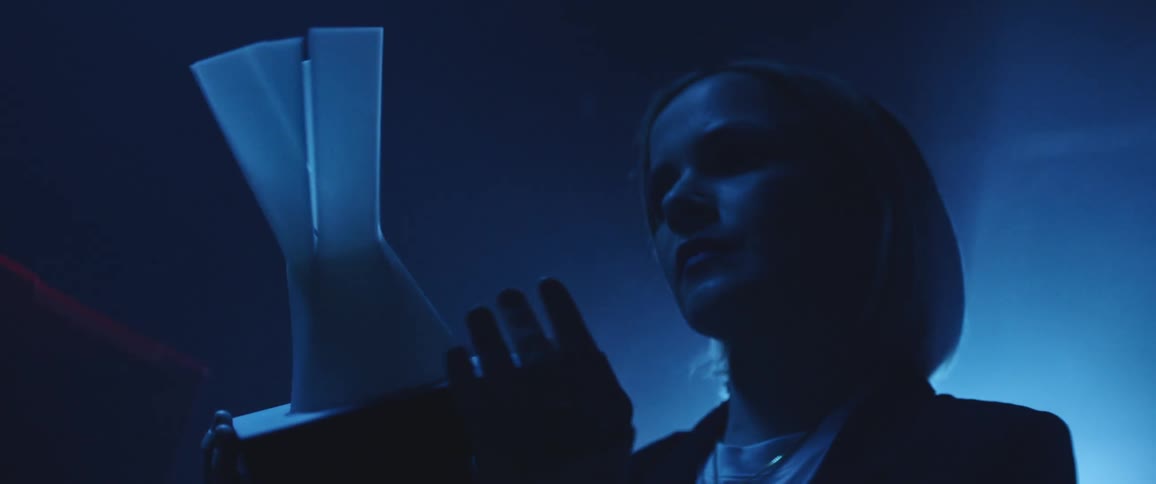 Woman examines model in dark room back lit by blue light